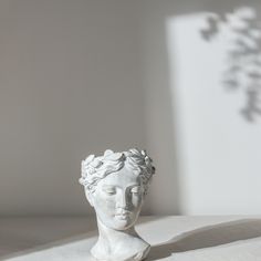 a white busturine sitting on top of a table next to a shadow cast wall