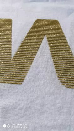 the letter m is made out of gold sequins on a white t - shirt