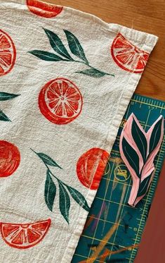 a piece of fabric with oranges and leaves on it next to a cutting board