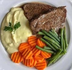 a white plate topped with meat, mashed potatoes and carrots next to green beans