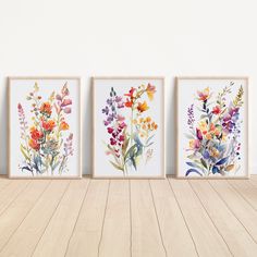 three watercolor flowers are displayed in front of a white wall with wooden flooring