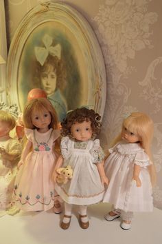 three dolls standing next to each other in front of a wall with pictures on it