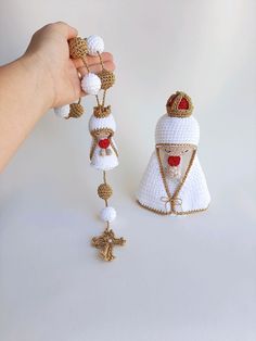 a hand is holding two christmas ornaments in white and gold, one with a red heart on it