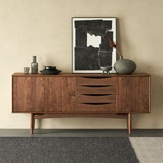 a wooden sideboard with two vases on top and an art piece above it