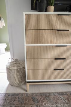 a white dresser sitting next to a plant in a living room on top of a rug