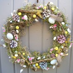 a wreath made out of moss, pine cones and other things is hanging on the wall