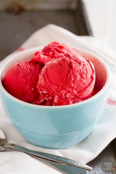 two scoops of red ice cream in a blue bowl on a white napkin next to a spoon