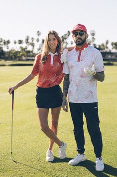 a man standing next to a woman on top of a lush green golf field holding a club