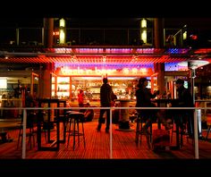 people are sitting at tables in front of a restaurant lit up with red and blue lights