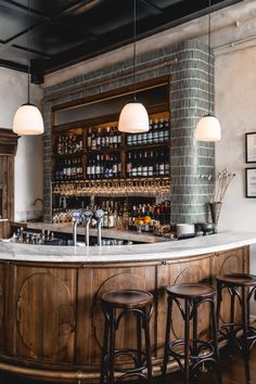 a bar with three stools in front of it and several bottles on the wall