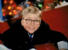 a young boy wearing glasses sitting on a red chair in front of a christmas tree