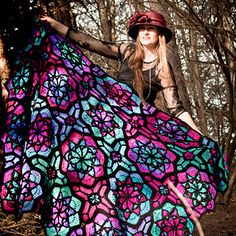 a woman in a hat and dress holding a colorful crocheted blanket while posing for the camera