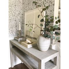 a white vase sitting on top of a wooden table next to a mirror and books