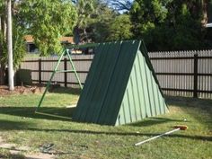 a green metal swing set sitting in the grass next to a wooden fence and trees