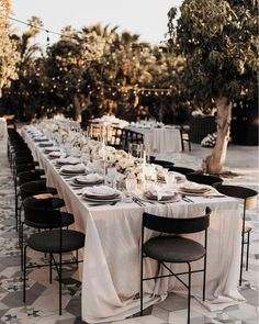 a long table is set up with black chairs and white linens for an elegant dinner