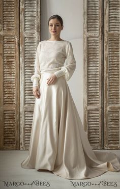 a woman standing in front of wooden doors wearing a long white dress with puffy sleeves