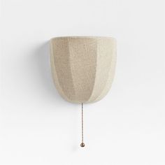 a white wall mounted light with a chain hanging from it's side and a beige shade