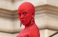 a woman with red paint on her face and body standing in front of a building