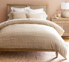 a bed with beige linens and pillows in a pink room next to a lamp