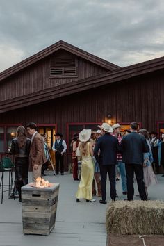 a group of people standing in front of a barn with a fire pit and hay bales