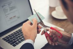 a man is cutting through a credit card with scissors on his lap top computer screen