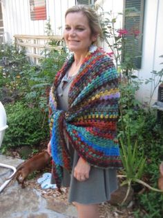 a woman wearing a multicolored crocheted shawl in front of her house