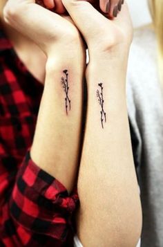 two women with matching tattoos on their arms, both holding each other's hands