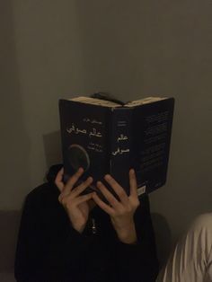 a person sitting down reading a book with their hands on top of the book cover