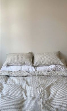 an unmade bed with two pillows on top of it and white walls in the background