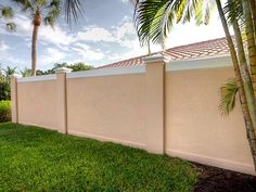 a fenced in area with grass and palm trees on the other side, next to a house