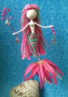 a doll sitting on top of a pink flower next to a sea urchin and seashell