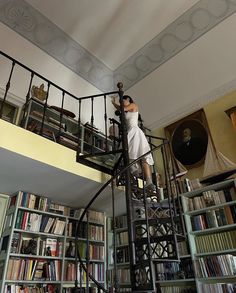 a woman standing on top of a spiral staircase in front of a bookshelf