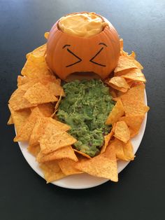 a white plate topped with chips and a pumpkin shaped bowl filled with guacamole