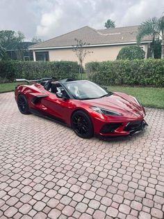 a red sports car is parked in front of a house with a driveway and bushes