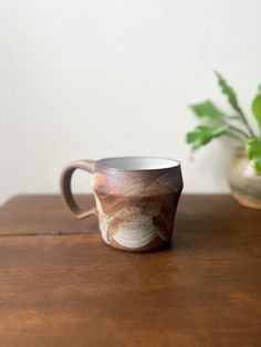 a coffee cup sitting on top of a wooden table next to a potted plant