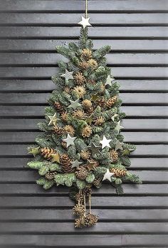 a christmas tree made out of pine cones and other decorations is hanging on the wall