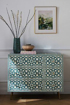 a blue and white chest of drawers next to a vase with some flowers on it