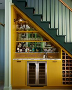 a kitchen with yellow cabinets under a stair case next to a wine rack filled with bottles and glasses