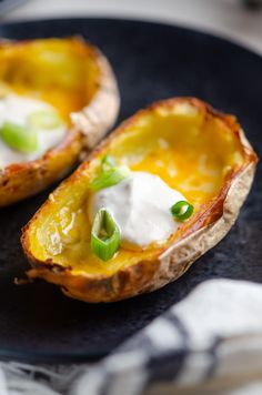 two baked potato halves with sour cream and scallions on a black plate, ready to be eaten