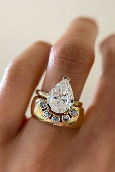 a woman's hand holding a gold ring with a pear shaped diamond on it