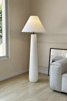 a white lamp sitting on top of a wooden floor next to a chair and window