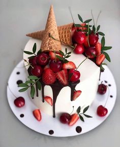 a cake decorated with strawberries and cherries is on a white plate next to an ice cream cone