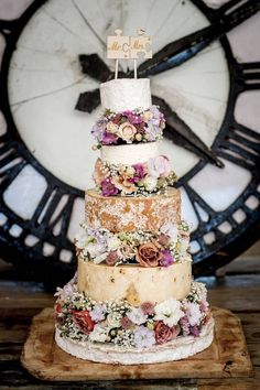 a multi layer cake with flowers on it and a clock in the backround