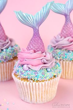 three cupcakes with pink and blue frosting on them, one is shaped like a mermaid tail