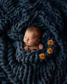 a newborn baby is curled up in a blue blanket with yellow flowers on the side