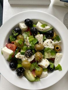 a salad with olives, cucumbers and feta cheese in a white bowl