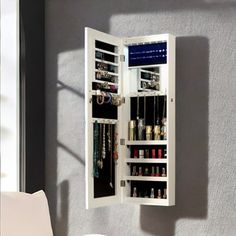 a white mirrored medicine cabinet with jewelry hanging from it's door and shelves on the wall