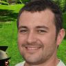 a man is smiling for the camera in front of a green yard and trees,