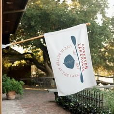 a white banner hanging from the side of a building next to a brick walkway and trees