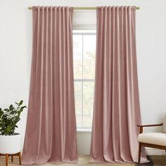 a living room with pink curtains and a chair in front of a window that has a potted plant next to it